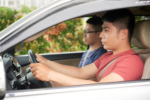 Вид сбоку уверенно азиатского человека за рулем автомобиля со своим другом в качестве пассажира