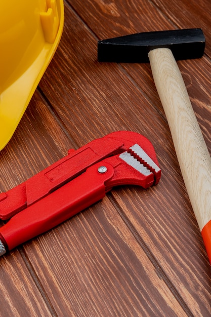 Side view of construction tools as brick hammer pipe wrench safety helmet on wooden background