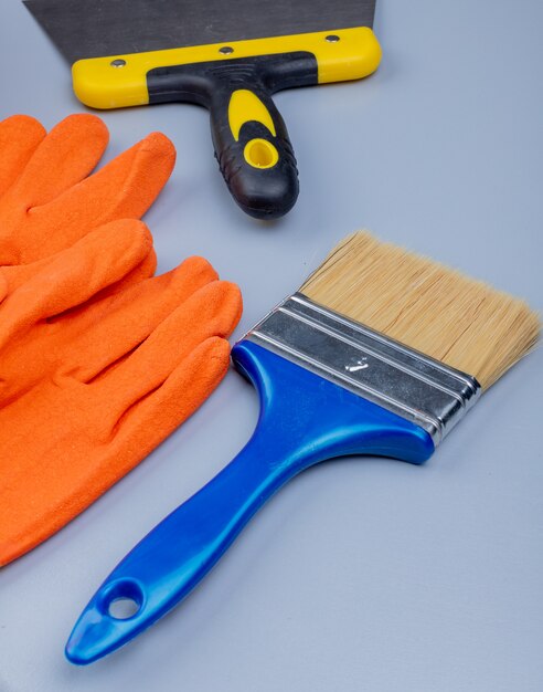 Side view of construction tools as gloves putty knife and paint brush on gray background