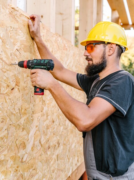 Side view of construction worker drilling in plywood