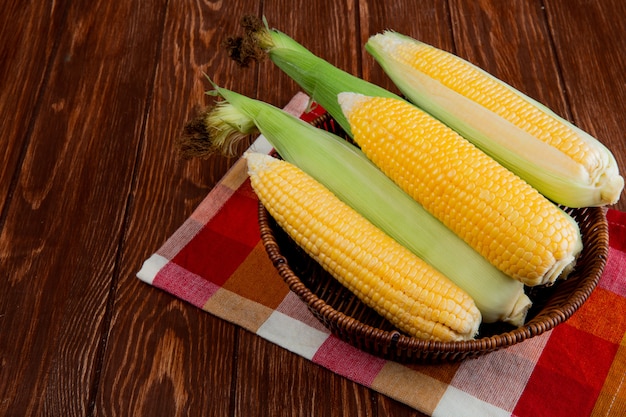 Side view of cooked and uncooked corns in basket on cloth and wooden table with copy space