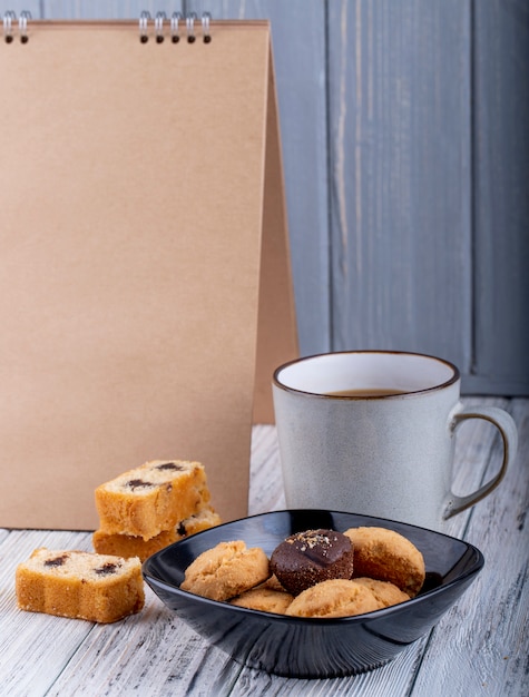 Side view of cookies in a black bowl and a cup with cocoa on wooden