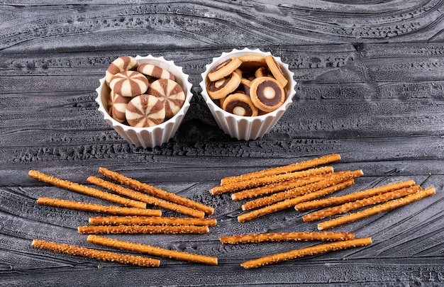 Side view of cookies in bowls and crackers on dark horizontal