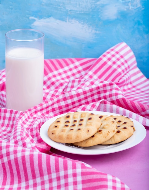 Side view of cookies on a white plate served with a glass of milk on pink