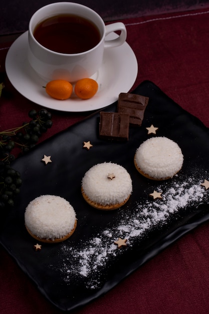 La vista laterale dei biscotti con i fiocchi della noce di cocco e il cioccolato su un bordo nero è servito con tè