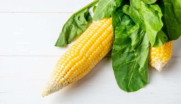 Free photo side view of corn cob and spinach on wooden surface