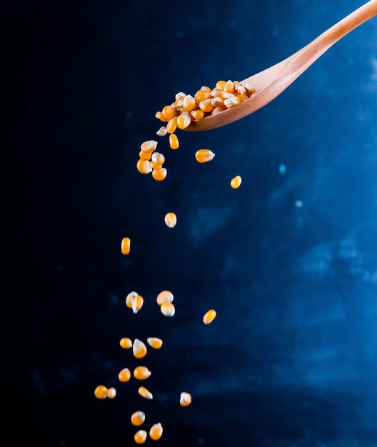 Free photo side view of corn seeds falling from a wooden spoon