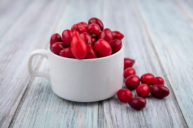 Side view of cornel berries in cup and on wooden background
