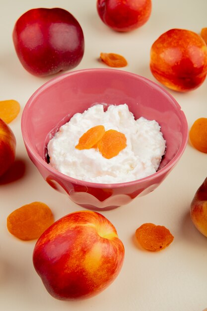 Side view of cottage cheese in a bowl and fresh sweet nectarines on white