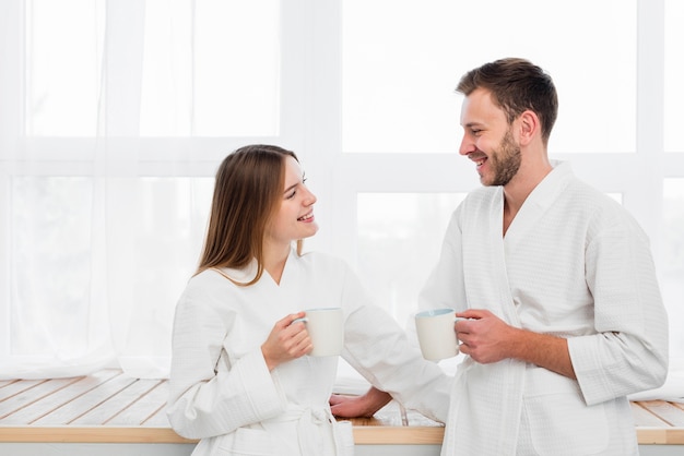 Side view of couple in bathrobes holding cups