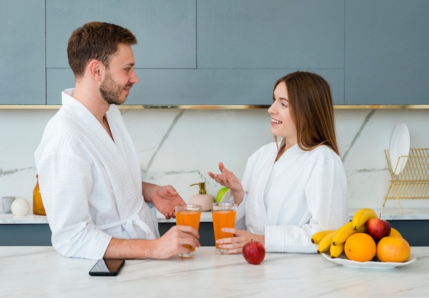 Free photo side view of couple in bathrobes with glasses of juice