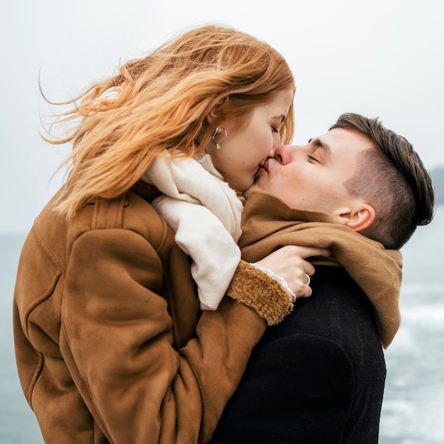 Side view of couple by the lake during winter kissing