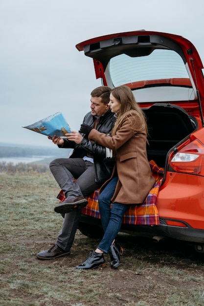 Side view of couple checking a map in the car's trunk outdoors