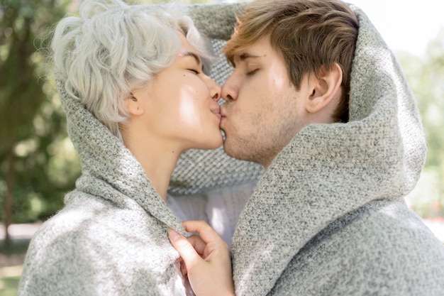 Side view of couple covered in blanker kissing outdoors
