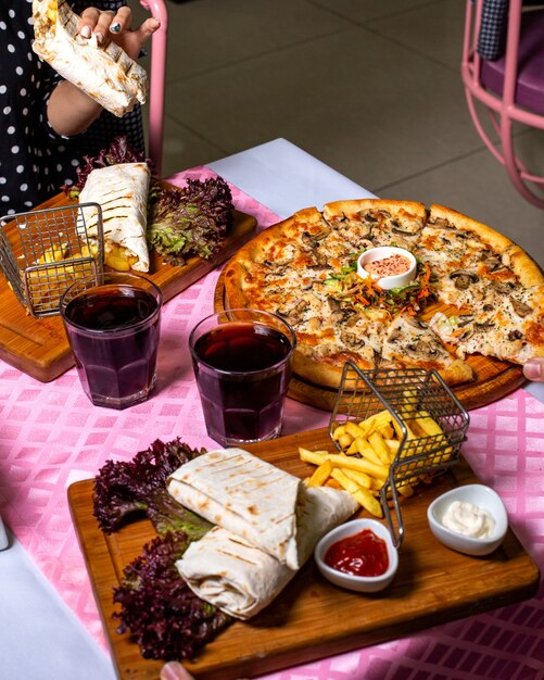 Side view of a couple eating pizza and doner wrapped in lavash served with french fries and sauces at the table at the table