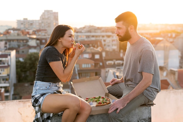 Free photo side view of couple eating pizza outdoors