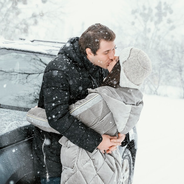 Side view of couple kissing in the snow while on a road trip