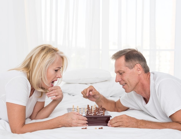 Free photo side view couple playing chess in the bedroom