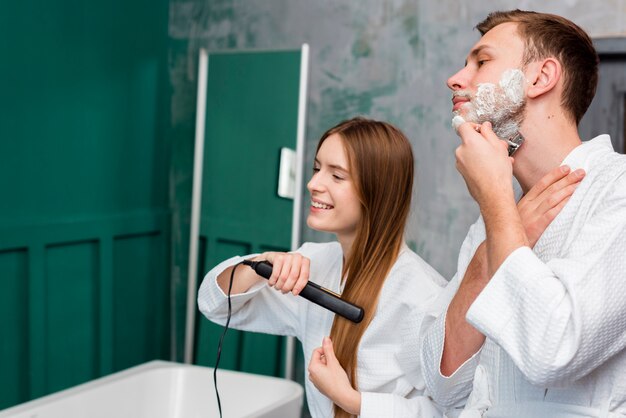 Side view of couple shaving and straightening hair