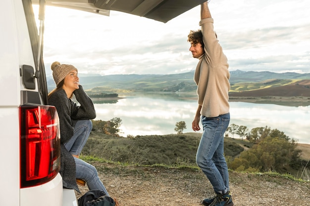 Free photo side view of couple sitting on the  trunk of the car while on a road trip