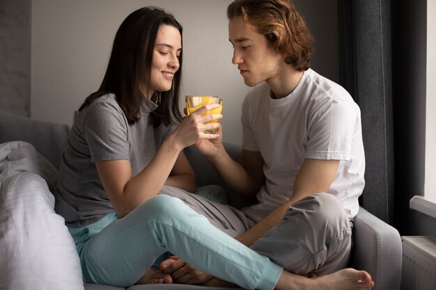 オレンジジュースのガラスを共有するソファの上のカップルの側面図