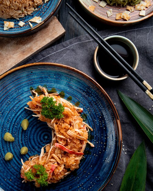 Side view of crab salad with vegetables and wasabi on a plate and soy sauce on black