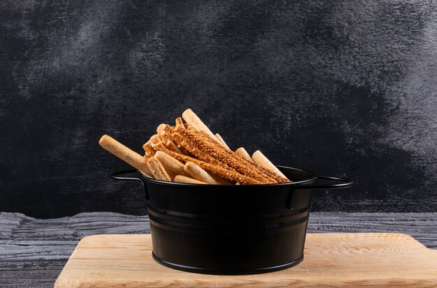 Foto gratuita vista laterale dei cracker in pentola nera e tagliere di legno sull'orizzontale scuro