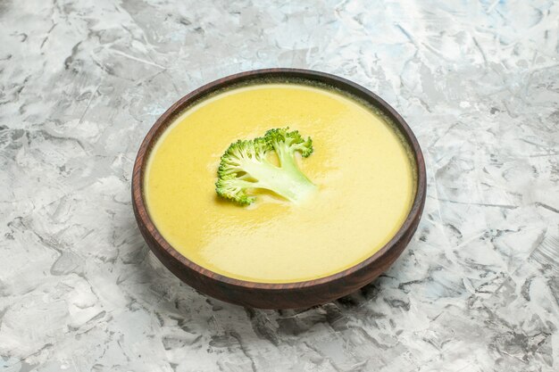 Side view of cream of broccoli soup in a brown bowl on white table