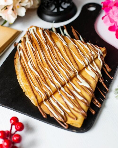 Side view of crepe with chocolate cocoa syrup on a wooden cutting board