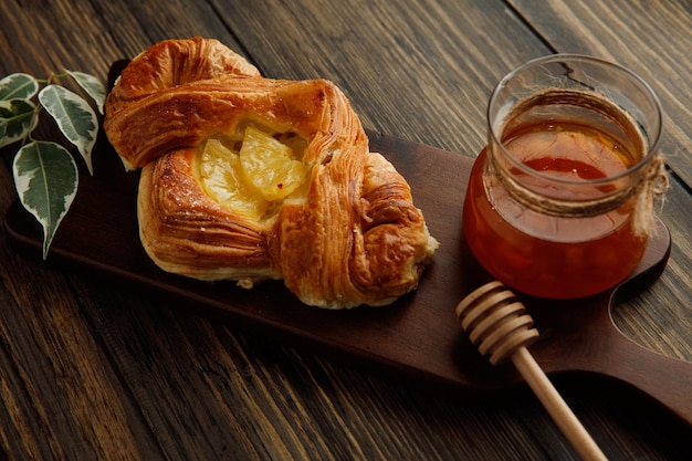 Side view of croissant and glass jar of jam with leaves on cutting board on wooden background
