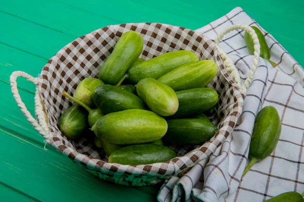 Side view of cucumbers in basket with other ones on cloth and green table