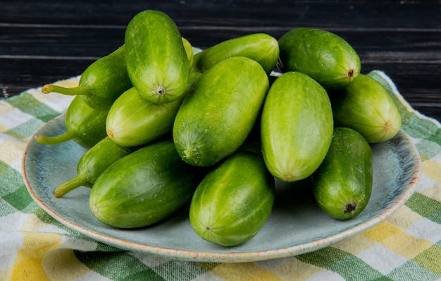 Free photo side view of cucumbers in plate on plaid cloth and wooden table