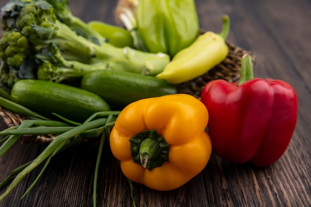 Free photo side view cucumbers with colored bell peppers  broccoli and green onions on wooden background