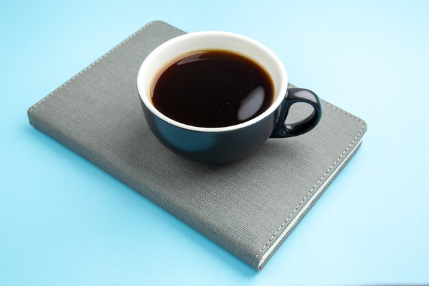 Side view of a cup of black tea on gray notebook on blue surface