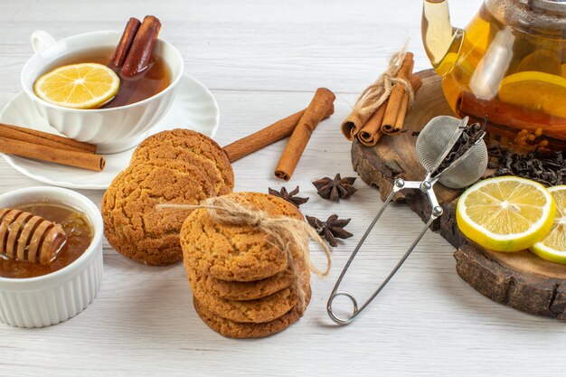 유리 냄비에 쌓인 쿠키 꿀과 허브 차, 흰색 배경에 있는 나무 쟁반에 다진 레몬 계피 라임의 측면 보기