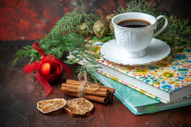 Side view of a cup of black tea on two books cinnamon limes and fir branches decoration accessory on dark background