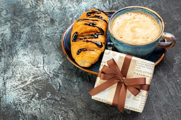 Side view of a cup of coffee and fresh delicious croisasant and gift on dark surface