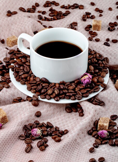 Вид сбоку чашки кофе с кофейными зернами и кубиками коричневого сахара