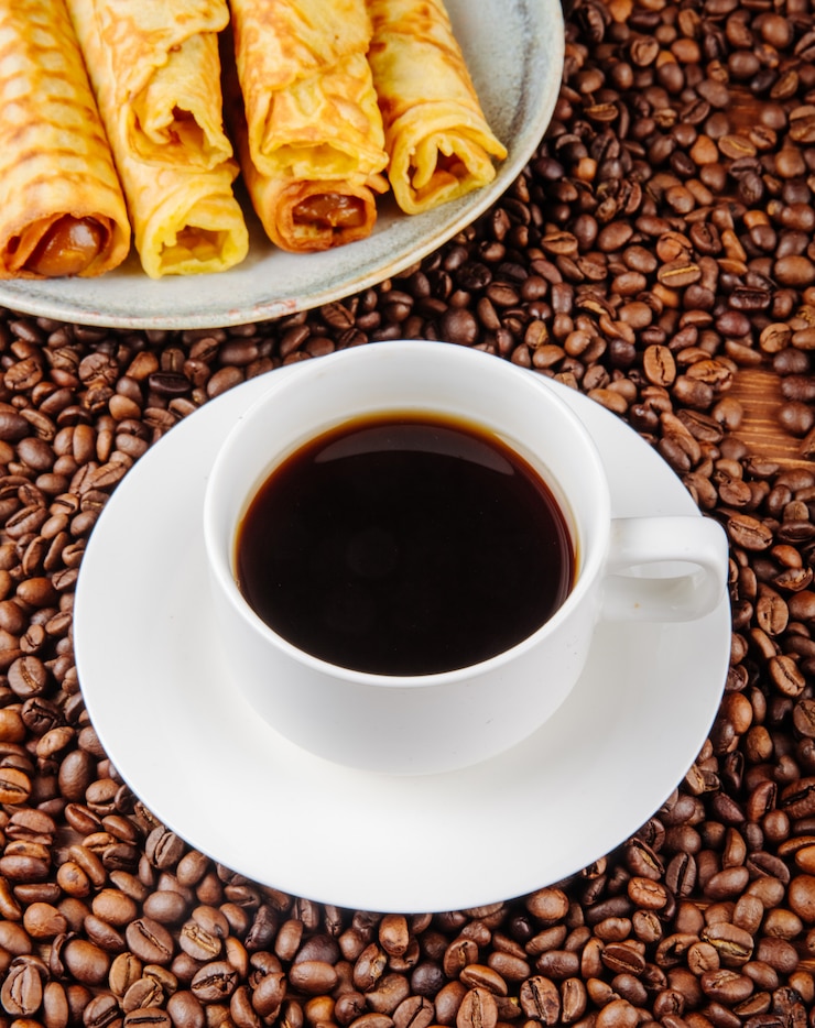 コーヒー豆のプレートにコンデンスミルクで満たされたウエハーロールとコーヒーのカップの側面図