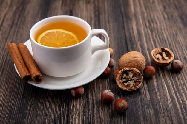 Side view of cup of hot toddy with cinnamon on saucer and nuts walnuts on wooden background