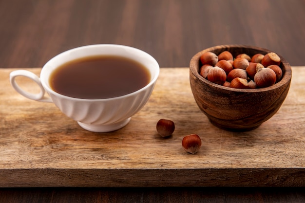 Vista laterale della tazza di tè e ciotola di noci sul tagliere su fondo in legno