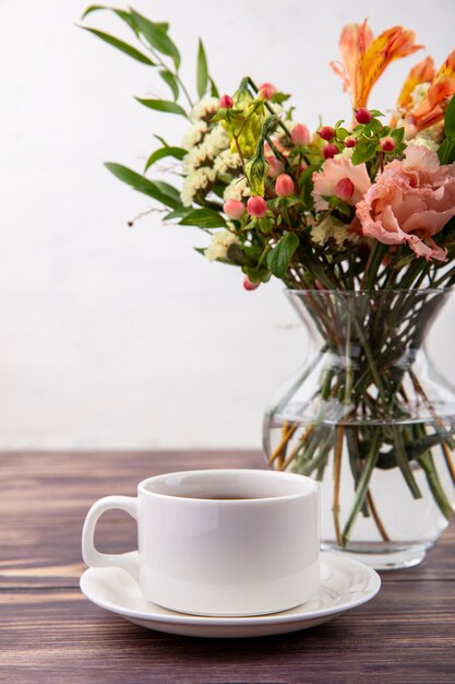 Side view of a cup of tea with beautiful flowers on a glass vase on a wooden table on white wall