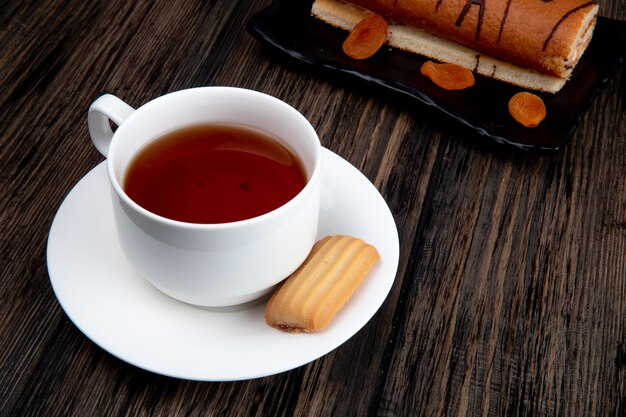 素朴な木製の表面のトレイ上のビスケットとロールケーキとお茶のカップの側面図