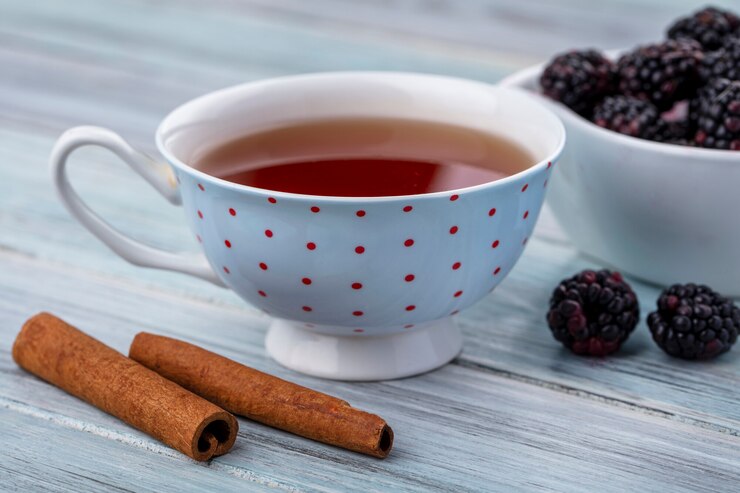 Free Photo side view of cup of tea with cinnamon and blackberry on a gray surface
