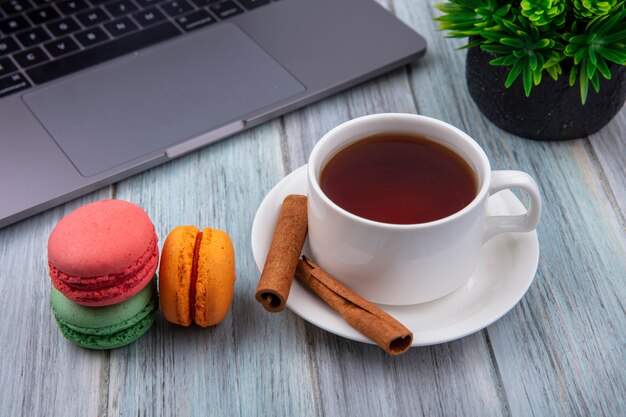 Side view of cup of tea with cinnamon colored macarons and a laptop on a gray surface