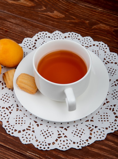 Vista laterale della tazza di tè con i biscotti in bustina di tè e albicocche su fondo di legno