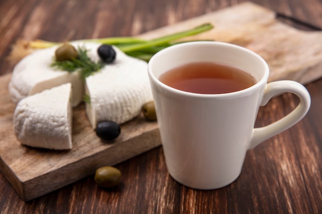 Side view cup of tea with feta cheese  with olives and green onions on a stand on a wooden background