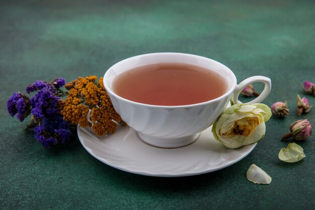 Side view cup of tea with flowers on green background