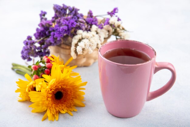 Side view of cup of tea with flowers on white surface