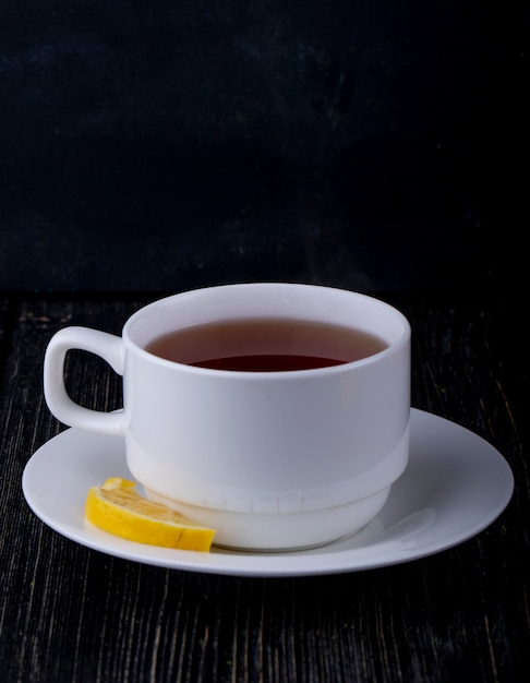 Side view of a cup of tea with lemon slice on black